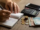 Pessoa anotando preços e calculando ganhos de renda extra em um caderno com calculadora ao lado